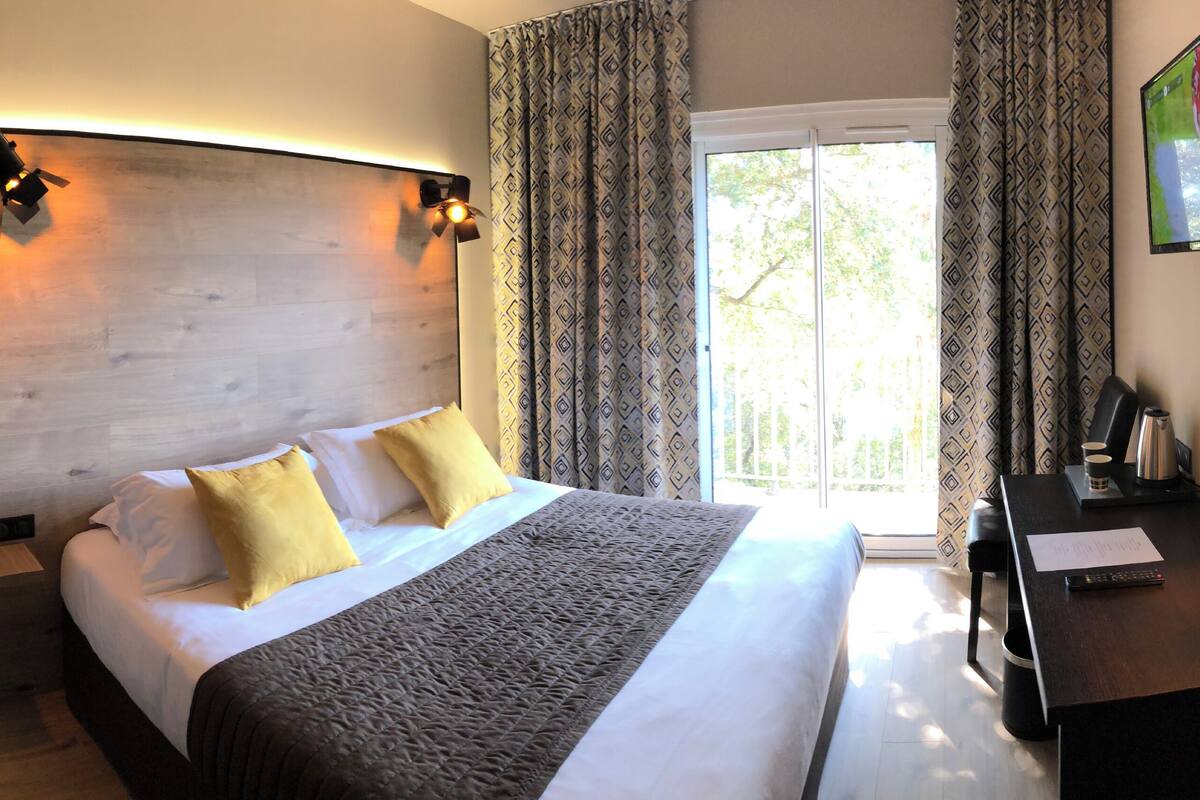Una habitación de hotel con una cama grande, un escritorio con lámpara y una televisión en la pared.