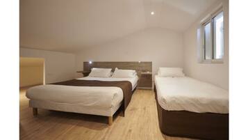 A bedroom with two beds, a wooden floor, and a window.
