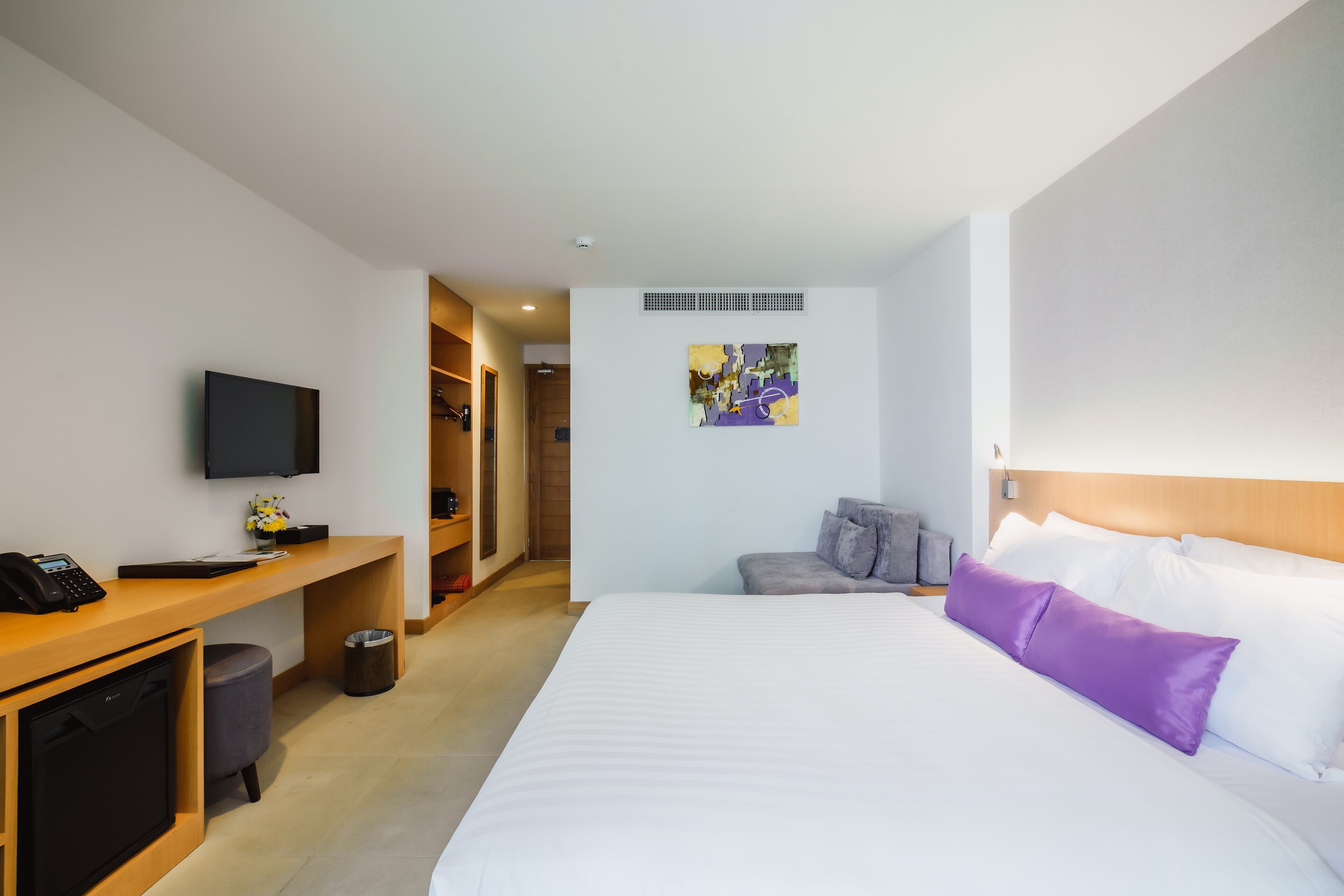 A hotel room with a bed, a desk with a phone, a television, and a painting on the wall.
