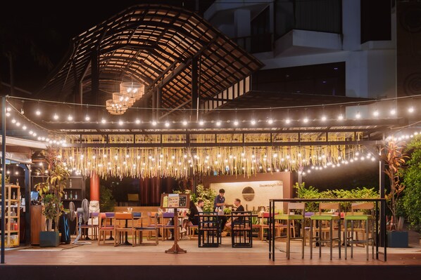 An outdoor dining area with tables and chairs, a covered seating area, and string lights. - The Lunar Patong (Patong)