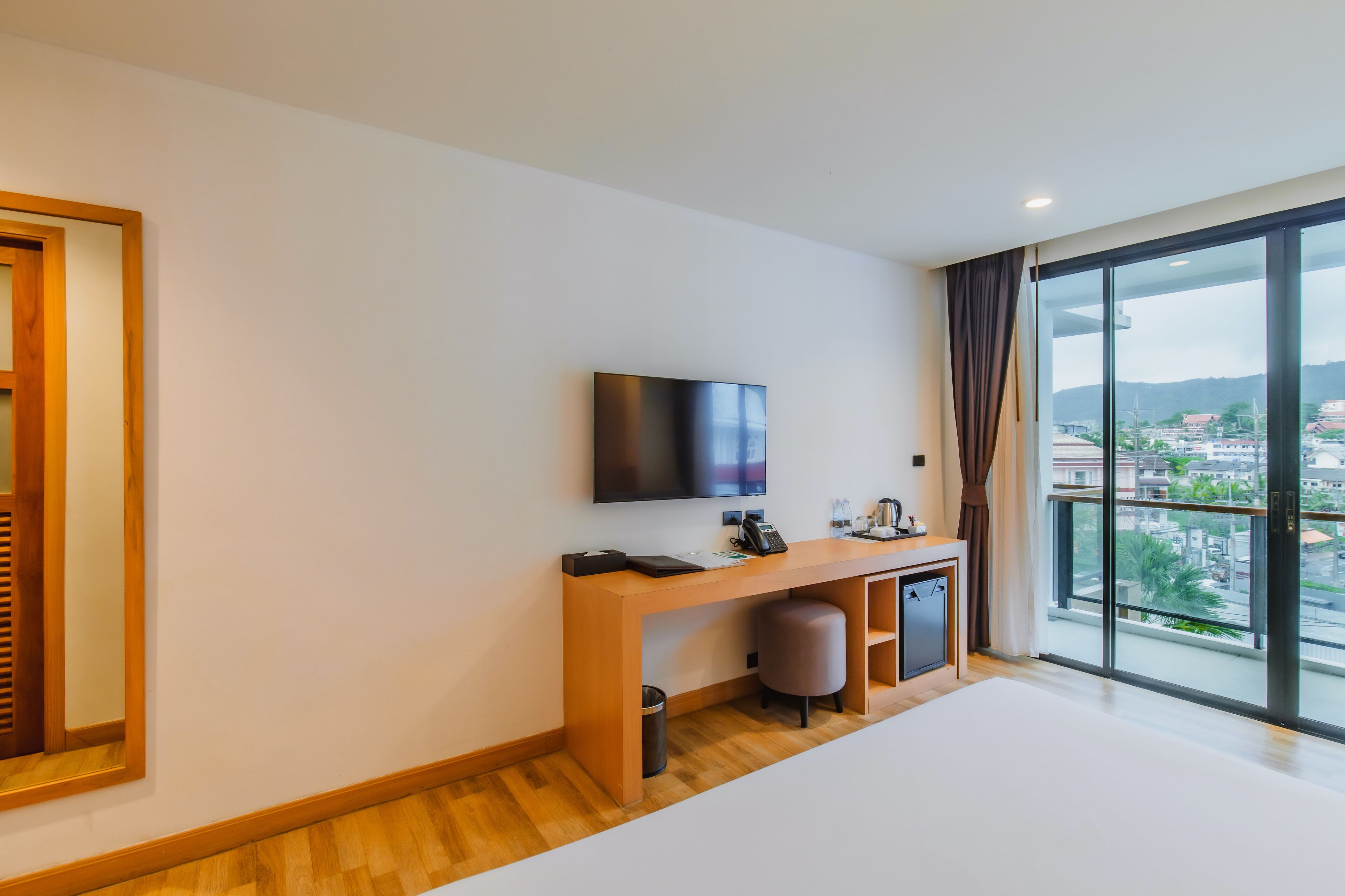 Habitació d'hotel moderna amb un gran finestral, televisió de pantalla plana, escriptori de fusta i una petita zona de seients.
