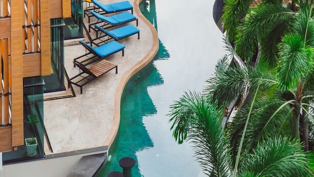 A modern hotel with a pool, lounge chairs, and palm trees. - The Lunar Patong (Patong)