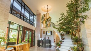 A spacious lobby with a reception desk, a staircase with plants, and large windows allowing natural light. - The Lunar Patong (Patong)