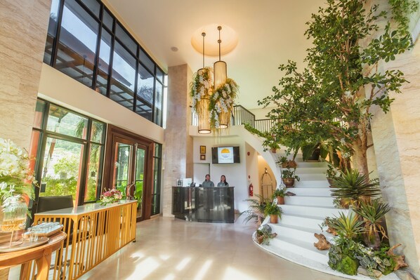 A spacious lobby with a reception desk, a staircase with plants, and large windows allowing natural light. - The Lunar Patong (Patong)