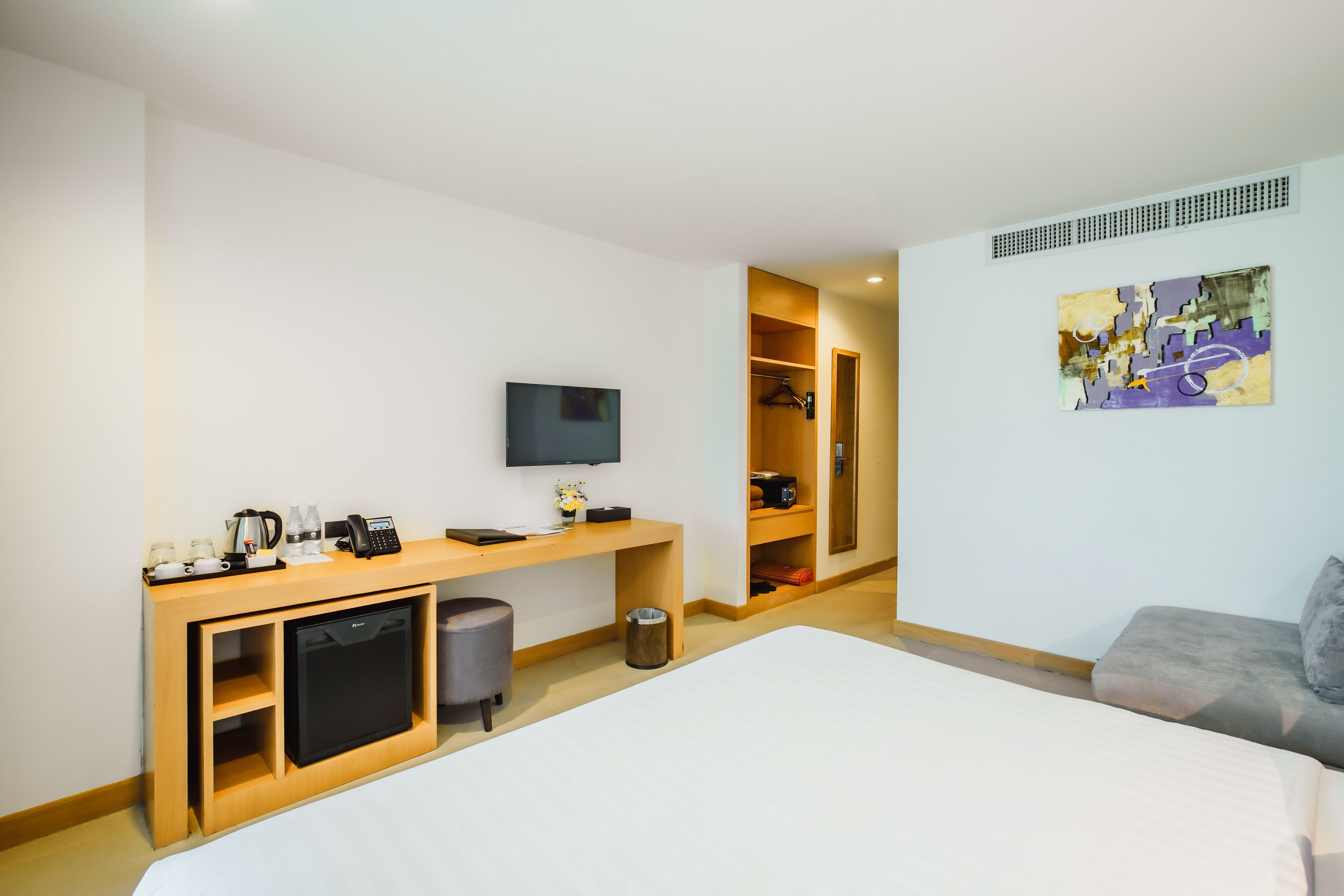 Habitación de hotel con cama, escritorio con televisor, cafetera y refrigerador pequeño.