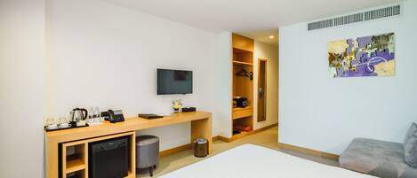 Habitación de hotel con cama, escritorio con televisor, cafetera y refrigerador pequeño.