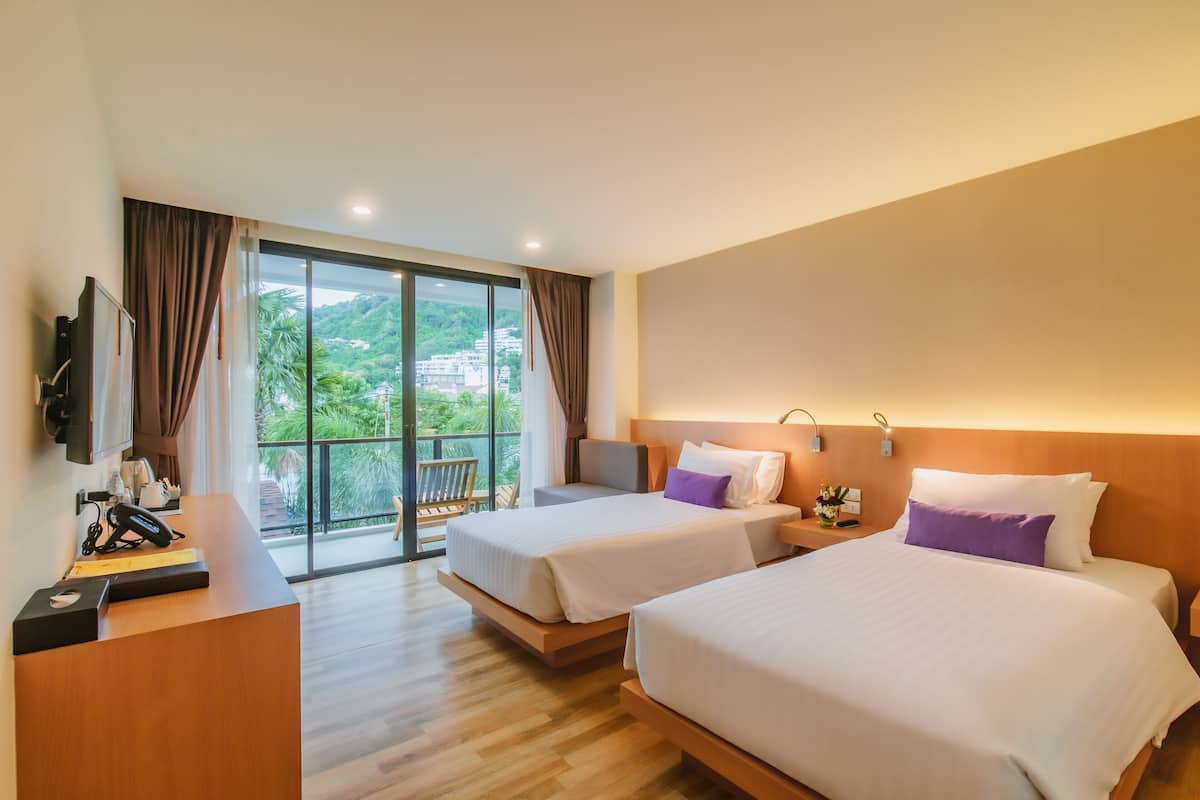 Une chambre d’hôtel avec deux lits, un bureau, un téléphone et une vue sur la verdure et les bâtiments.