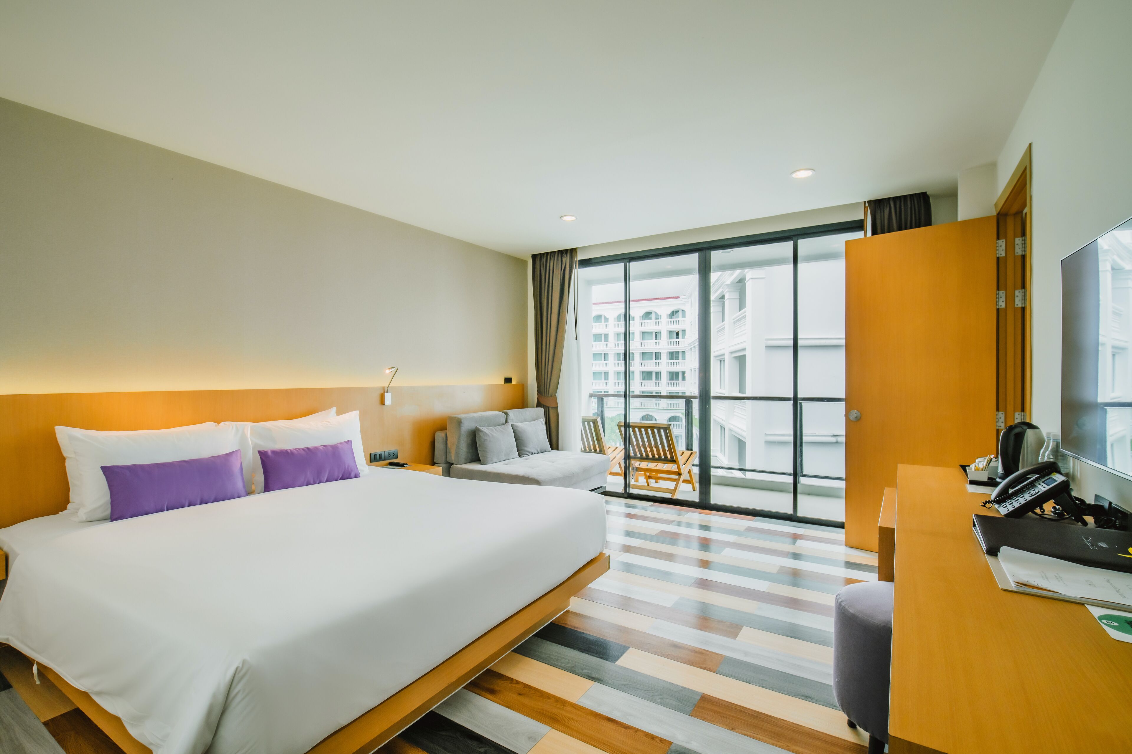 Habitación de hotel con una cama grande, un escritorio con teléfono y vistas de la ciudad a través de amplios ventanales.