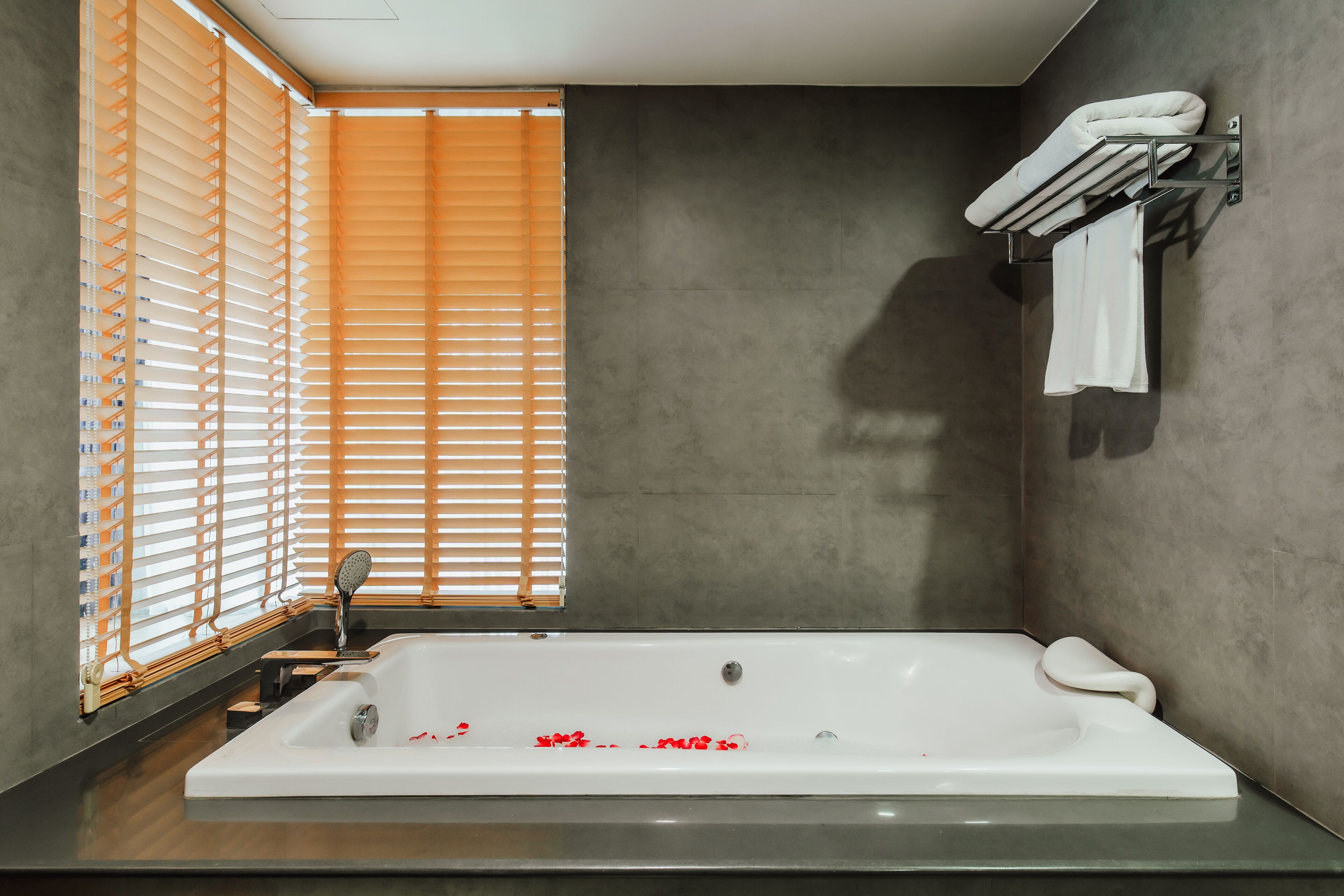 Un baño moderno con una bañera grande, un perchero y una ventana con persianas.