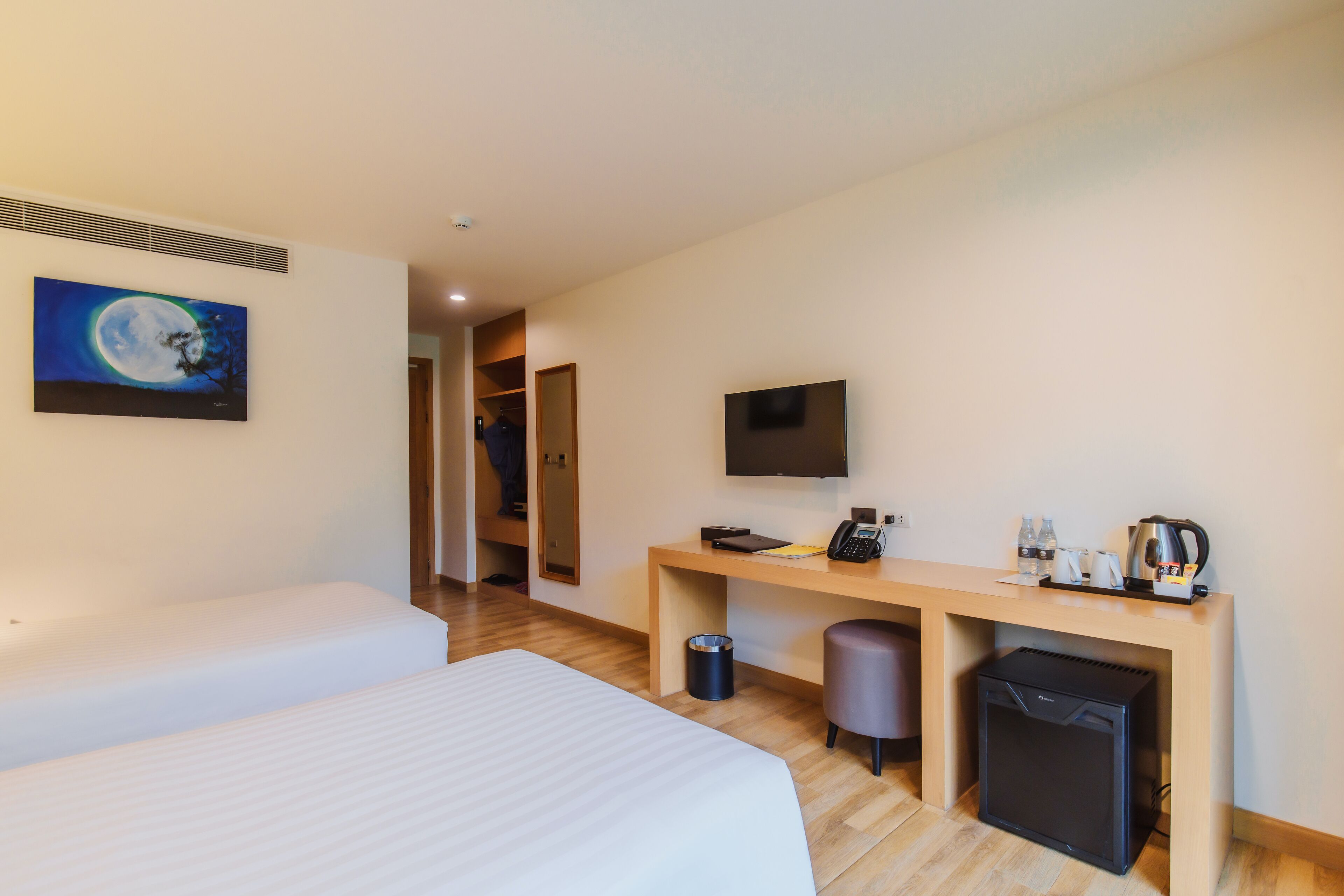 A hotel room with a bed, a desk with a TV, a small fridge, and a trash bin.