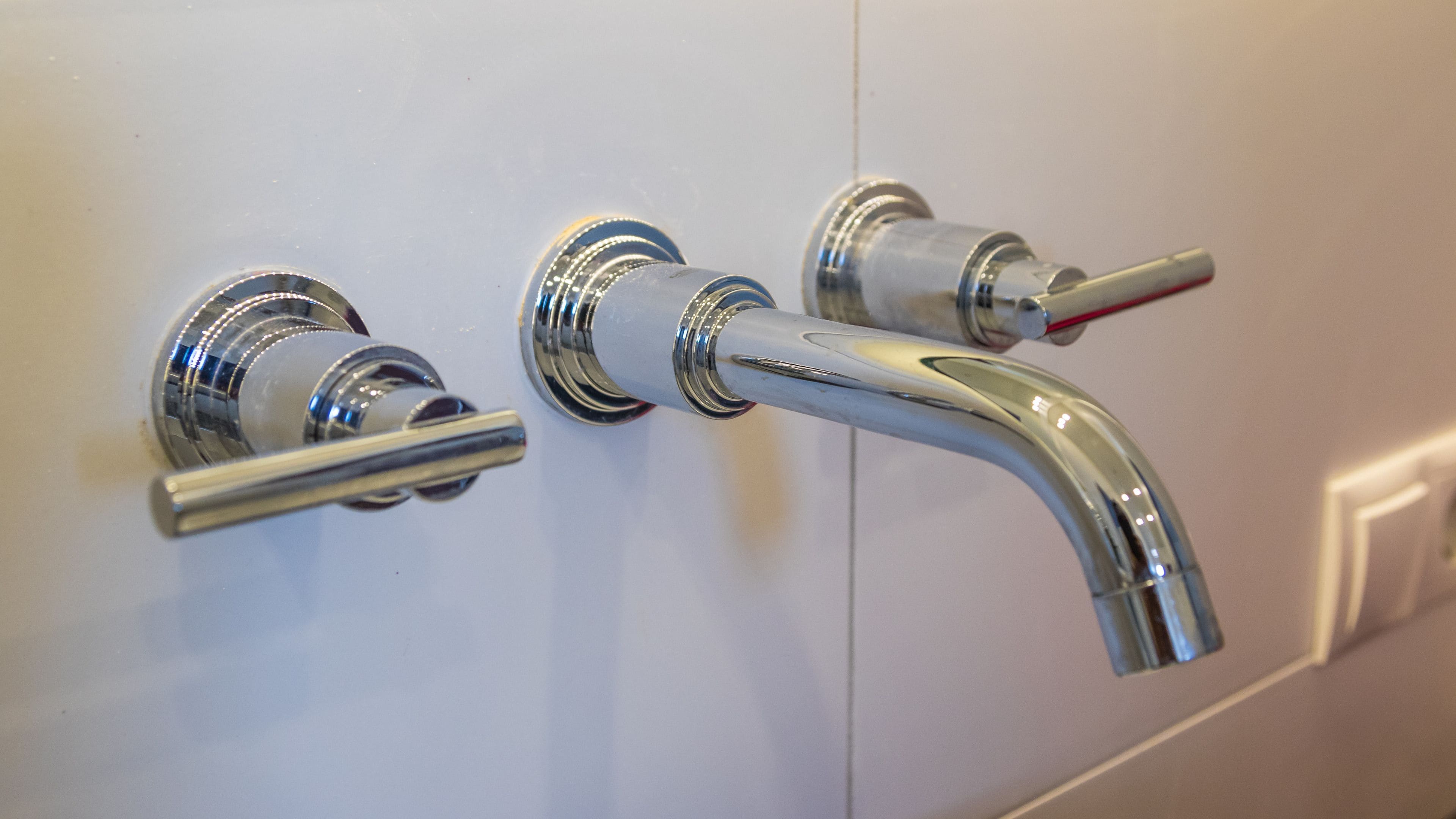 Un baño con lavamanos montado en la pared y dos llaves.