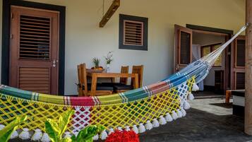 Una hamaca tendida entre dos puertas de madera, una mesa de madera con sillas y una pequeña planta en maceta.
