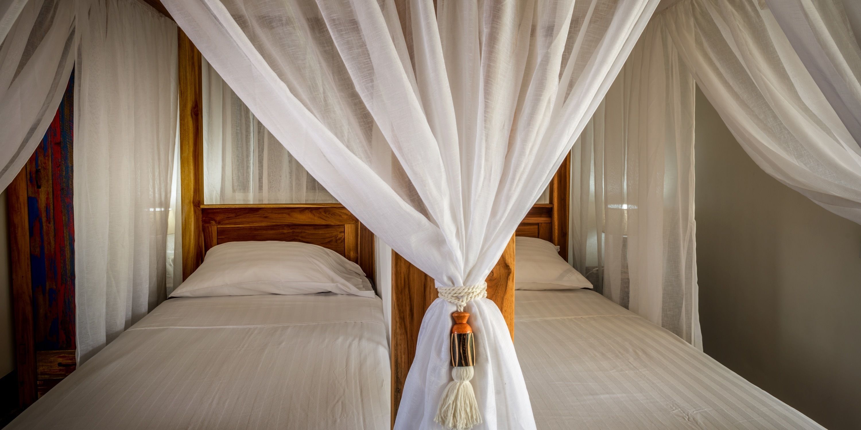 A room with two beds, each with white linens and wooden headboards.