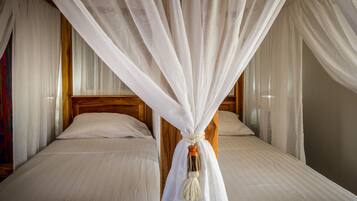 A room with two beds, each with white linens and wooden headboards.