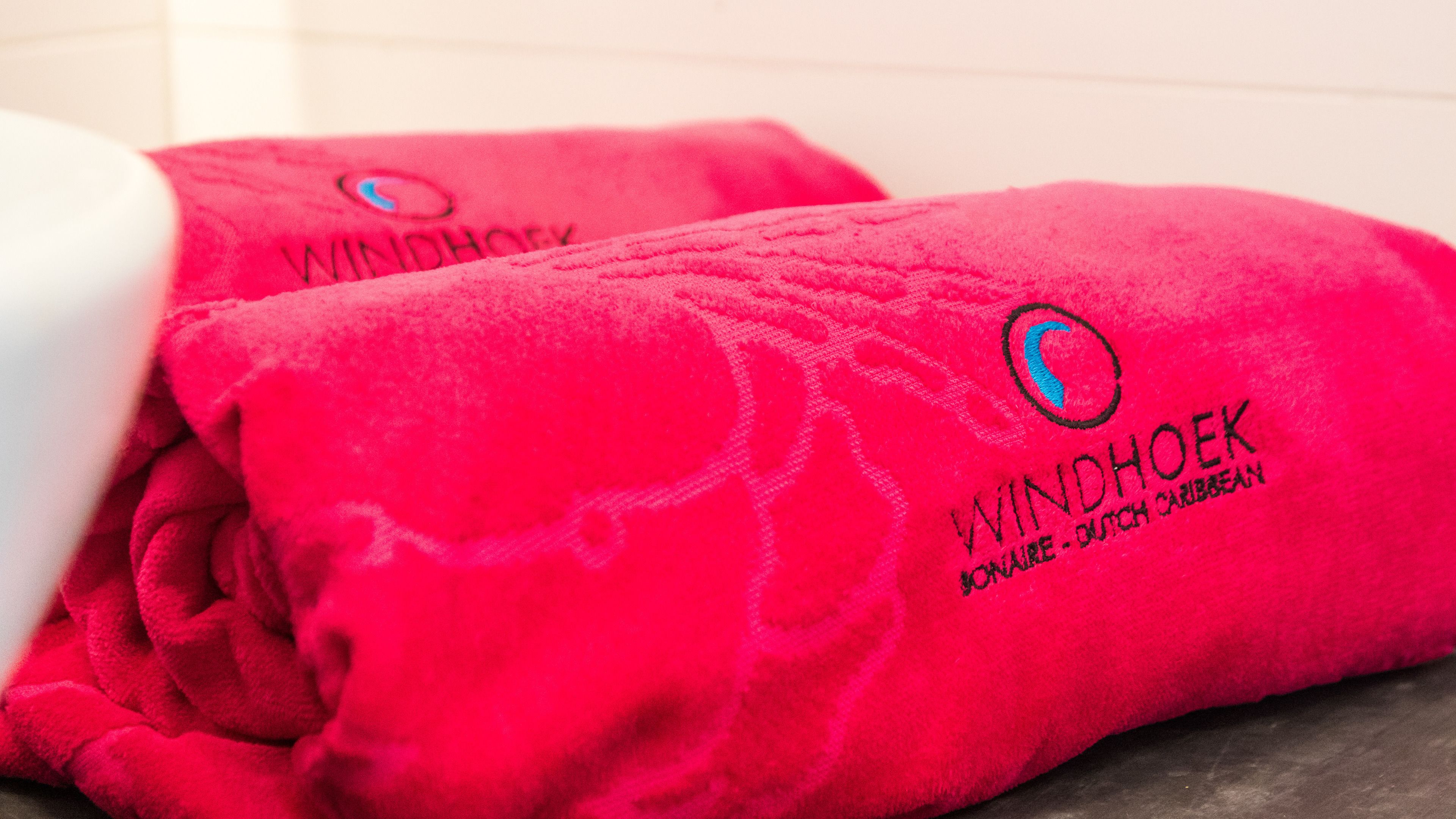 Zwei rote Handtücher mit der Aufschrift 'WINDHOEK' und 'MOANA - DUTCH CARIBBEAN'.