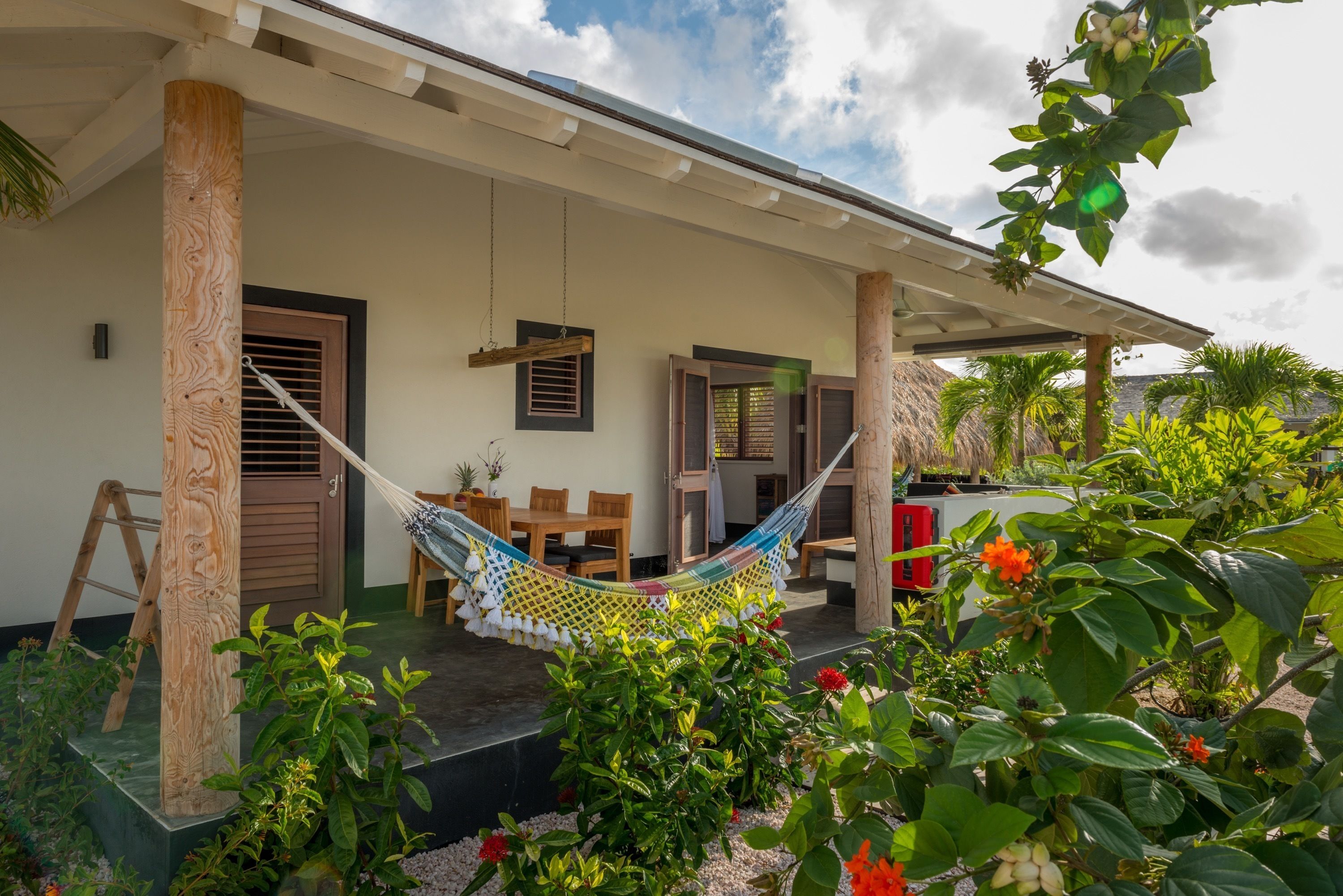 A covered outdoor area with a hammock, wooden furniture, and a small garden with plants and flowers.