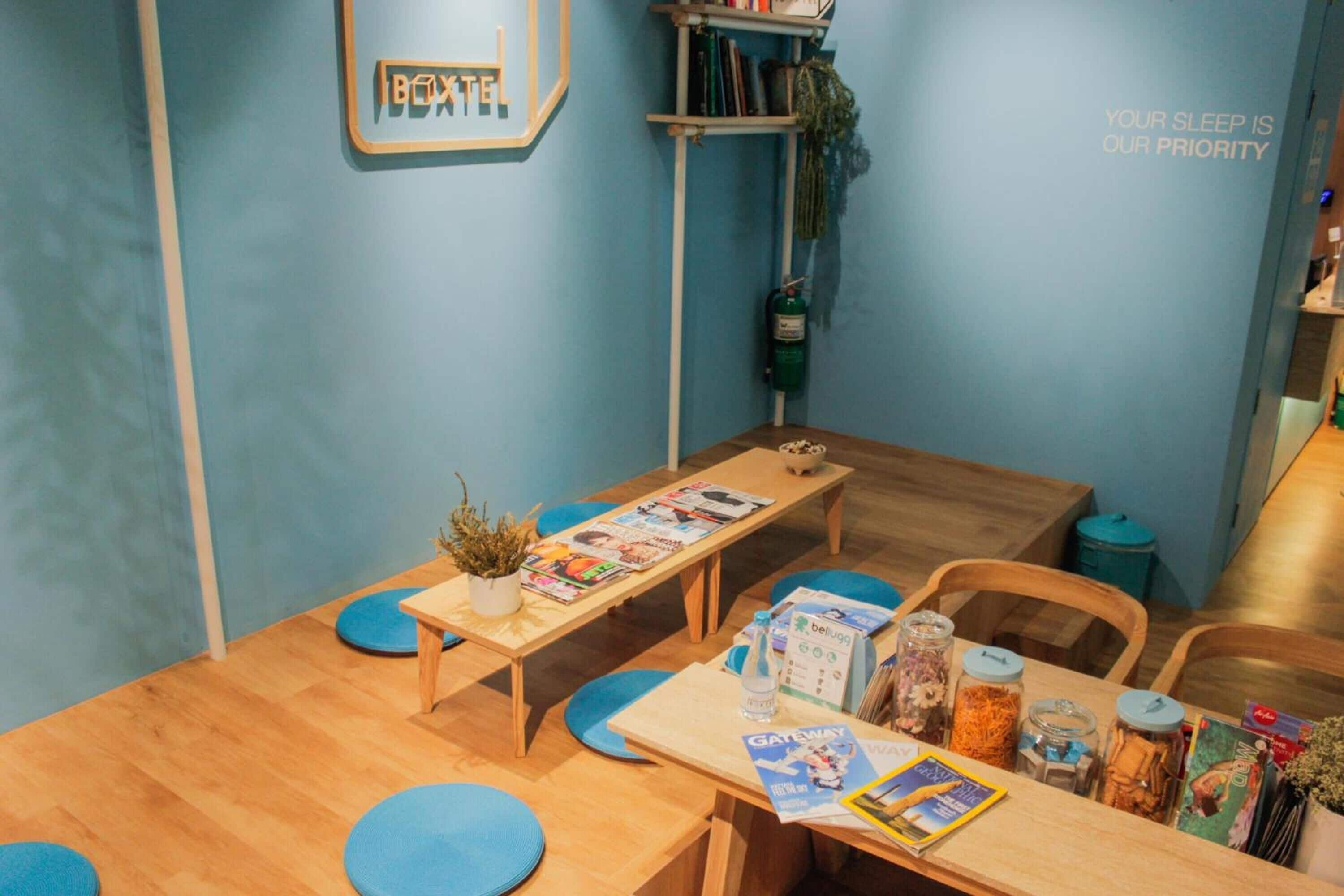 A cozy hotel room with a wooden table, blue chairs, and a bookshelf.