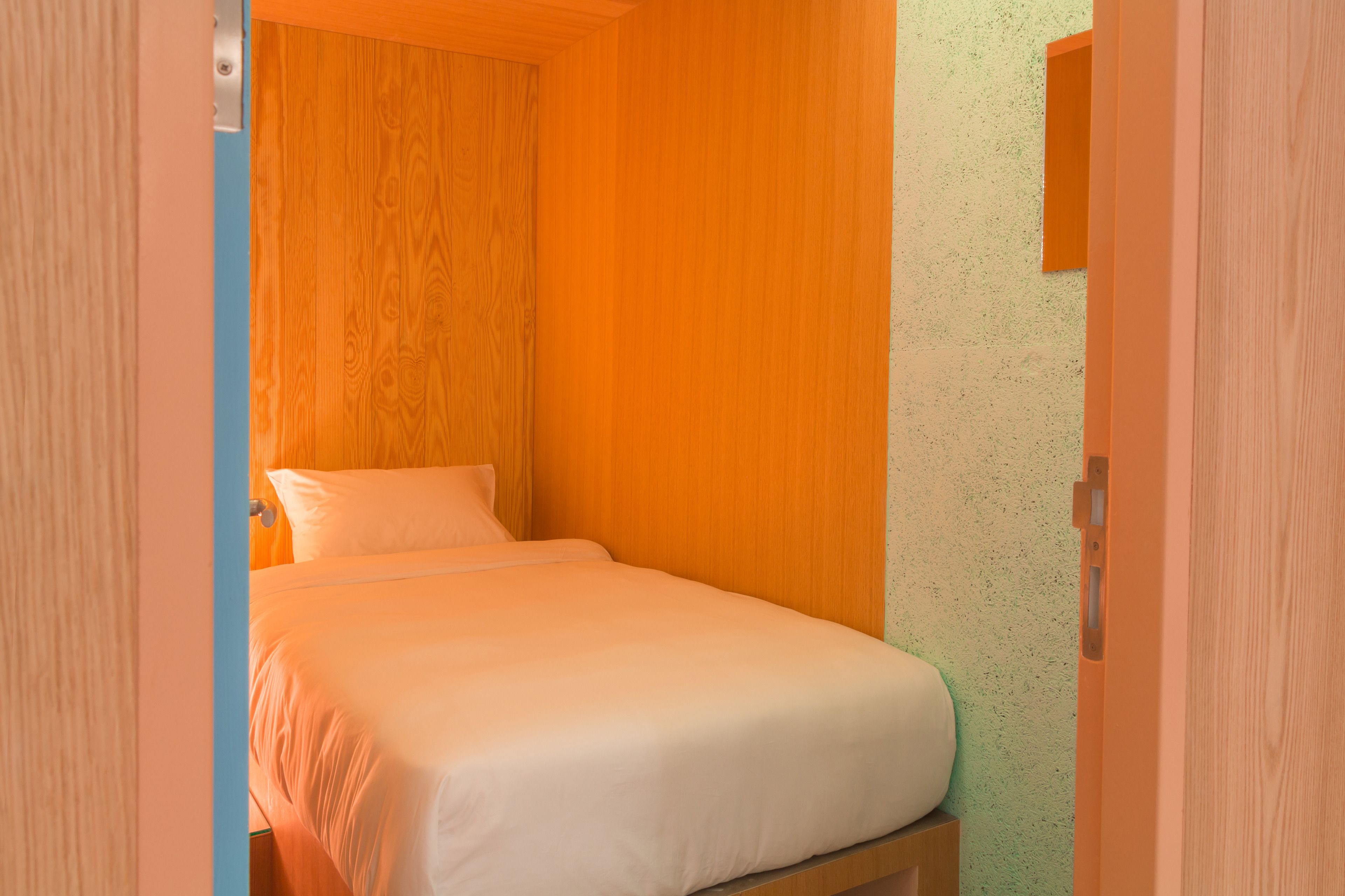 Ein kleines Zimmer mit einem Einzelbett, Holzwänden und einer Wand mit Grüner Struktur.