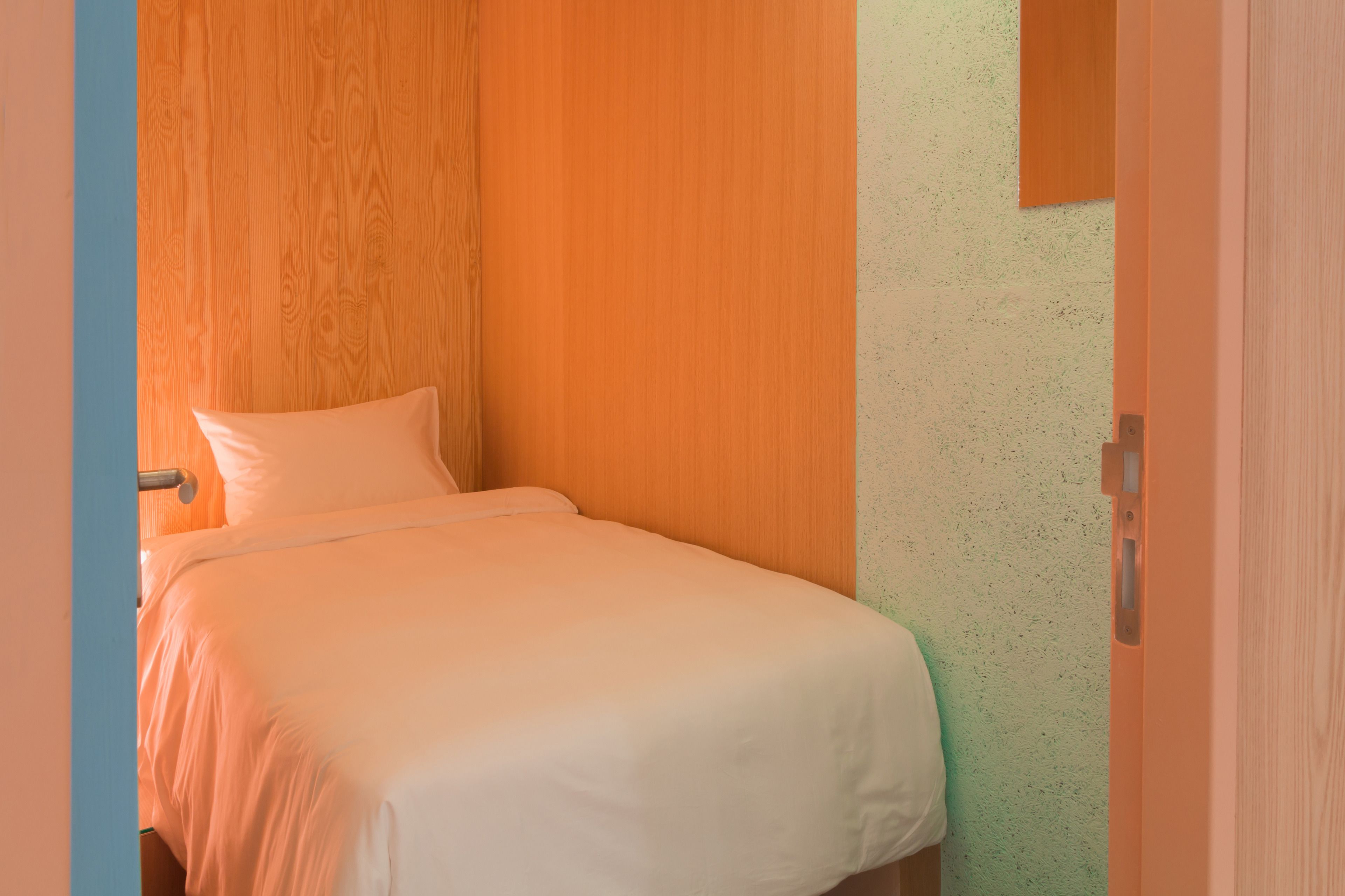 A single bed with white bedding in a room with wooden panel walls and a green textured wall.