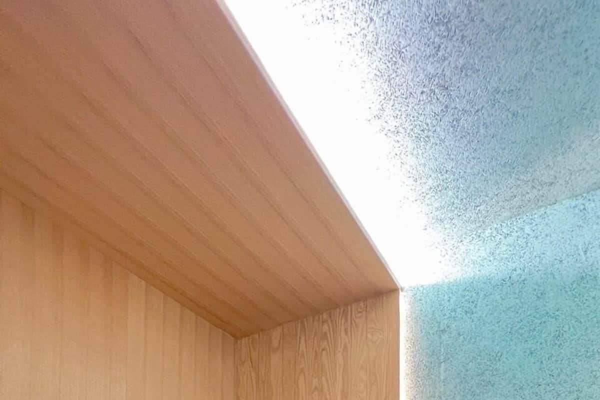 A single bed with a wooden headboard in a room with a sloped ceiling and a textured wall.