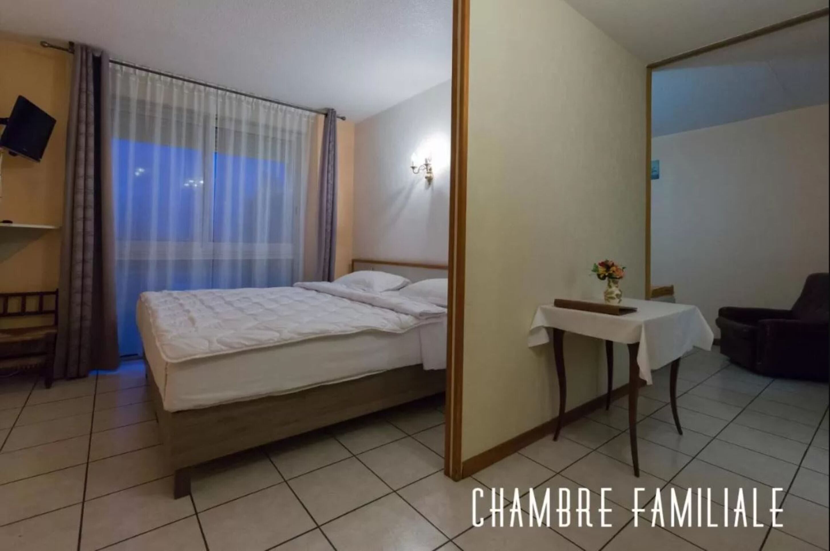 Une chambre à coucher avec un lit, une table de chevet ornée d’un vase, une chaise et un téléviseur posé sur une étagère.