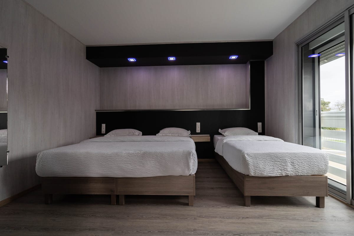 A modern bedroom with two beds, a dark headboard, and a large window.