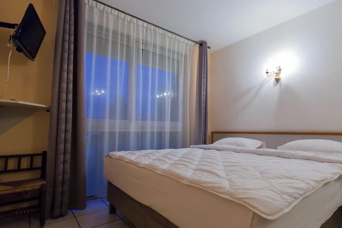 A hotel room with a bed, a TV mounted on the wall, and a window with curtains.