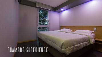 A hotel room with two beds, a window with a view of trees, and a ceiling light.