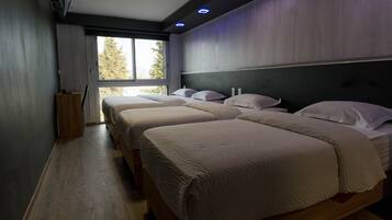 Een hotelkamer met drie bedden, een groot raam en een donker hoofdeinde.