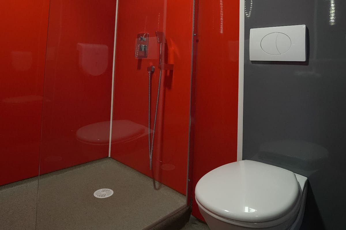 A bathroom with a shower, toilet, and a wall-mounted control panel.