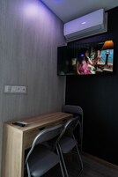 Una habitación con televisión en la pared, un escritorio de madera y una silla.