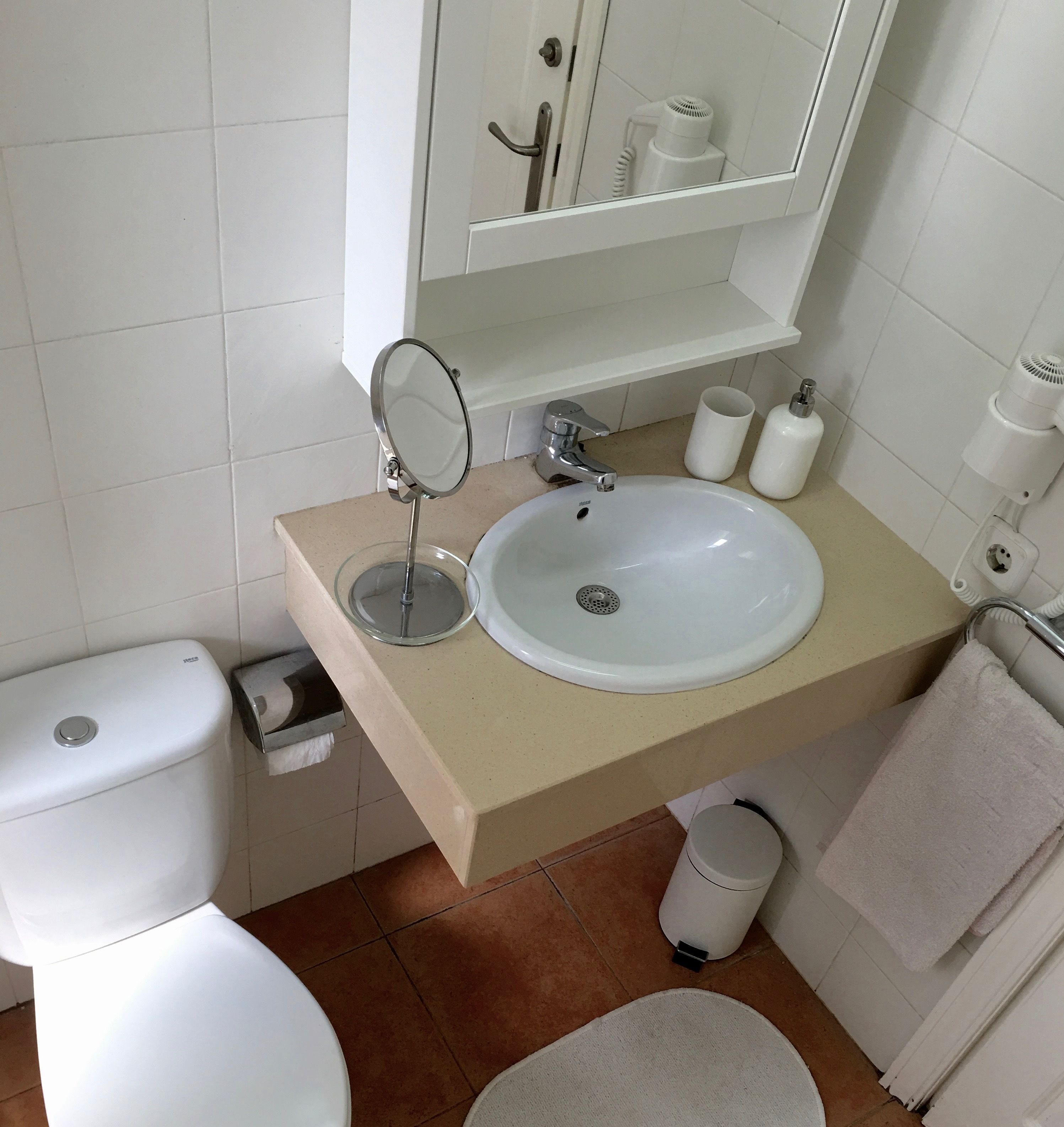 Kylpyhuone, jossa on valkoinen pesuallas, peili, wc-istuin ja roskakori.