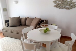 Un salón con sofá color crema, sillas blancas, una mesa con un tazón de manzanas y una decoración de peces en la pared.