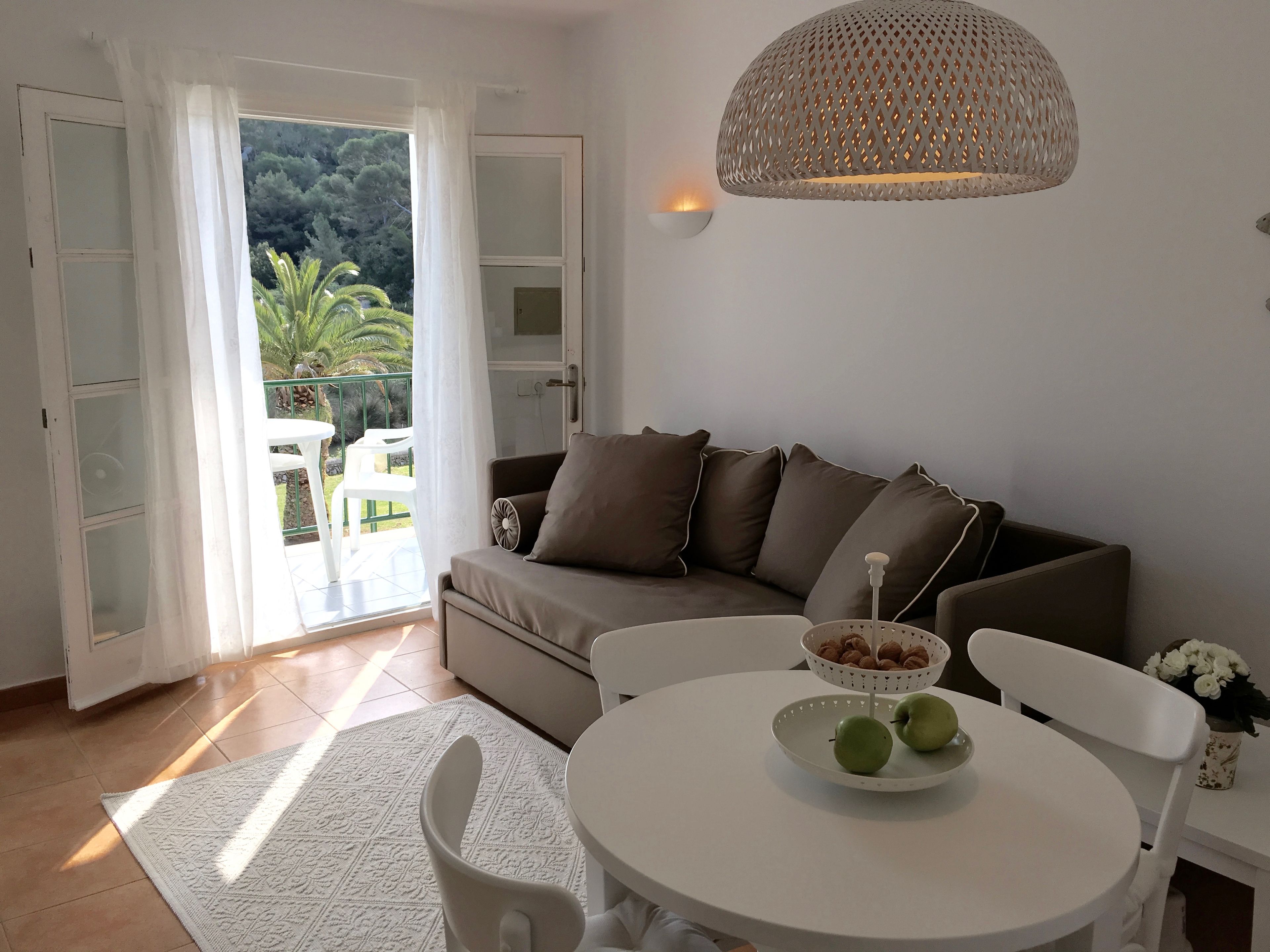 Un salon moderne avec un canapé, une table ronde sur laquelle on trouve des pommes et des noix, et un luminaire suspendu.