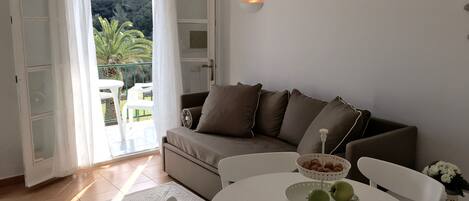A modern living room with a sofa, a round table with apples and nuts, and a hanging light fixture.