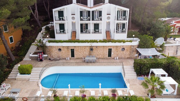 Un edificio moderno de dos plantas con piscina, mobiliario exterior y fachada de piedra.
