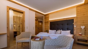 A cozy bedroom with a bed, two patterned armchairs, a small round table, and a wooden headboard.