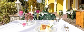 An outdoor dining area with tables set for two, surrounded by greenery and yellow walls. - Hotel Landgasthof Fischerwirt (Faistenau)