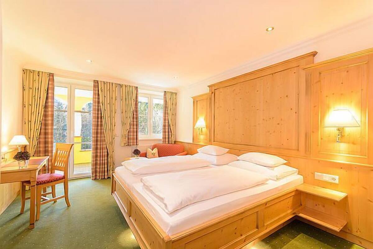 Una habitación de hotel con una cama de madera, un escritorio con una silla y una ventana con cortinas.