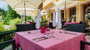 An outdoor dining area with pink tablecloths, white umbrellas, and wicker chairs.