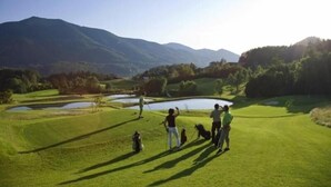 A golf course with a pond, mountains in the background, and people playing.
