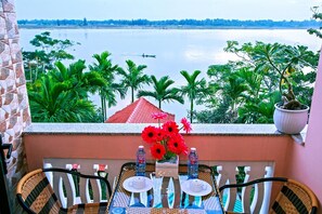 A balcony with a table set for two, overlooking a lake with a boat in the distance. - Thu Bon Riverside Homestay (Da Nang)