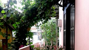 A narrow alleyway with a pink building on one side, covered with green vines and pink flowers. - Thu Bon Riverside Homestay (Da Nang)