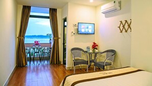 A hotel room with a balcony, a bed, a TV, and a table with chairs. - Thu Bon Riverside Homestay (Da Nang)