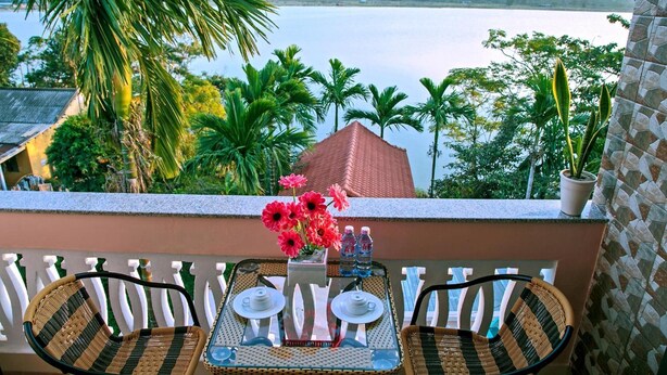 A balcony with wicker chairs, a table set with teapots and cups, and a vase of red flowers. - Thu Bon Riverside Homestay (Da Nang)