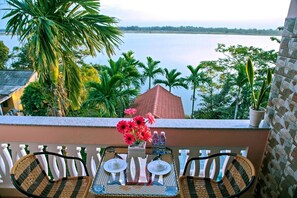 A balcony with wicker chairs, a table set with teapots and cups, and a vase of red flowers. - Thu Bon Riverside Homestay (Da Nang)