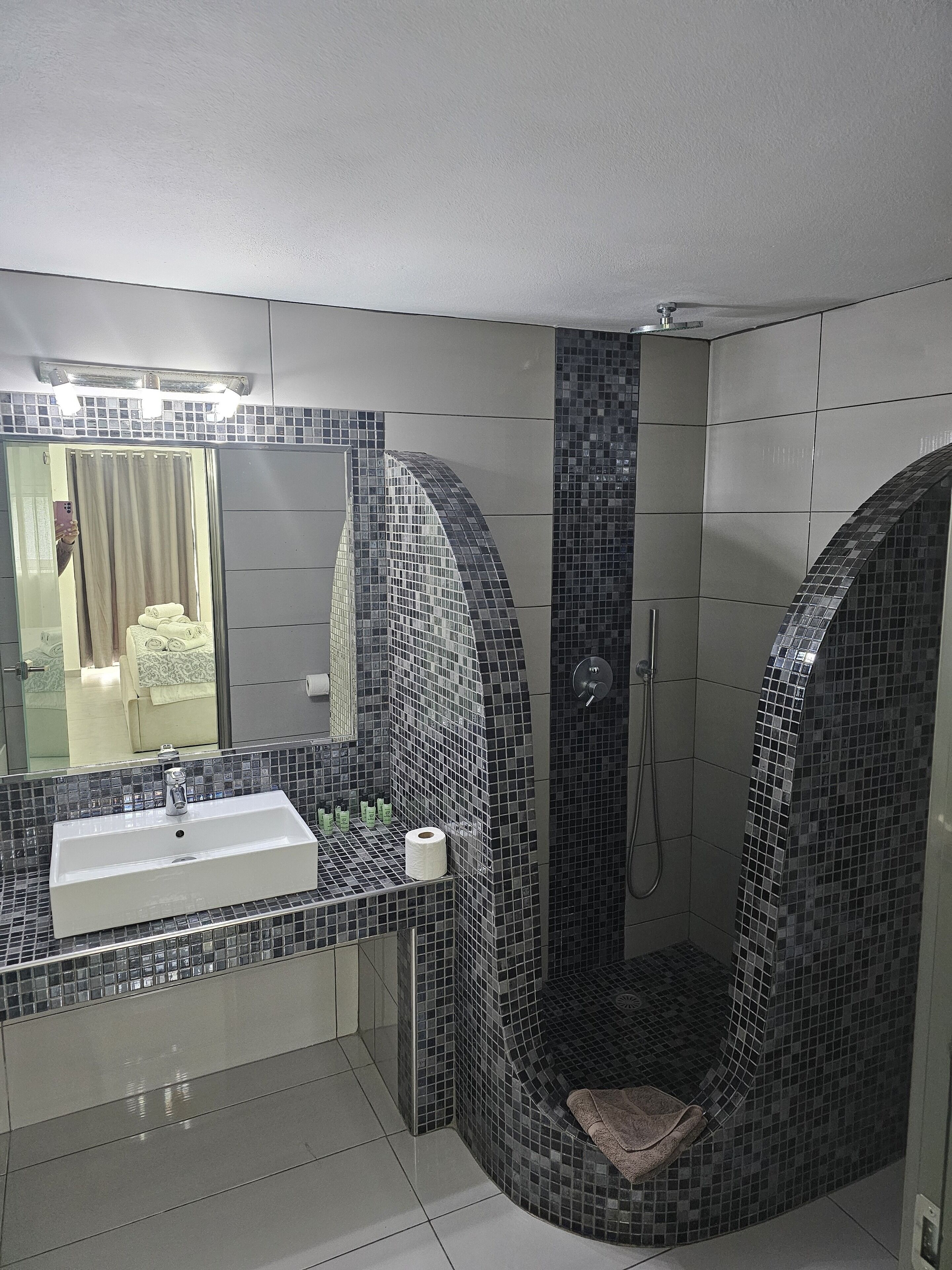 A modern bathroom with a large mirror, a sink, and a shower area with a tiled wall.