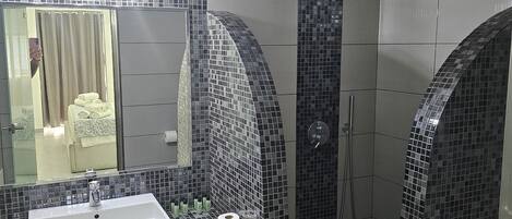 A modern bathroom with a large mirror, a sink, and a shower area with a tiled wall.