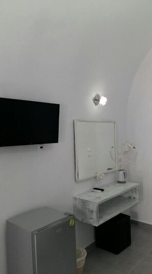 Un baño con lavamanos blanco, espejo y televisor negro montado en la pared.