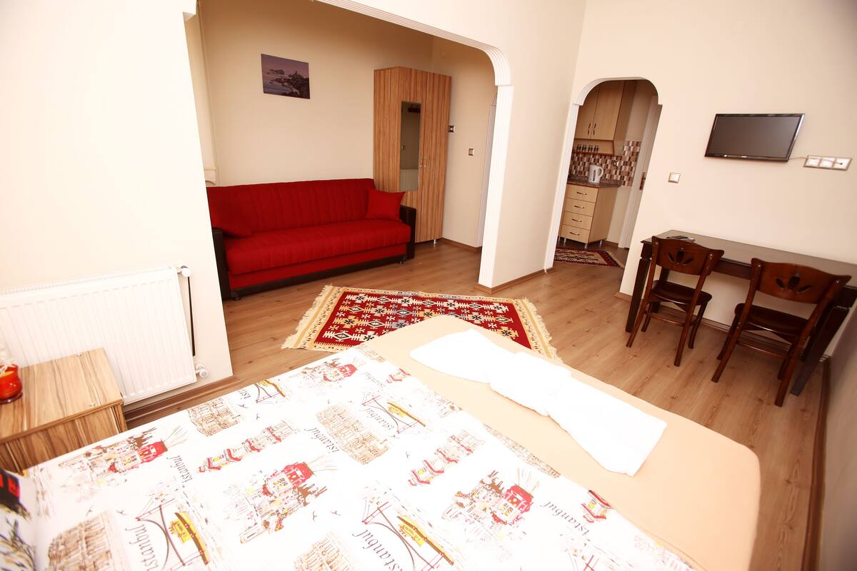 A bedroom with a bed, a red sofa, a wooden desk, and a TV.
